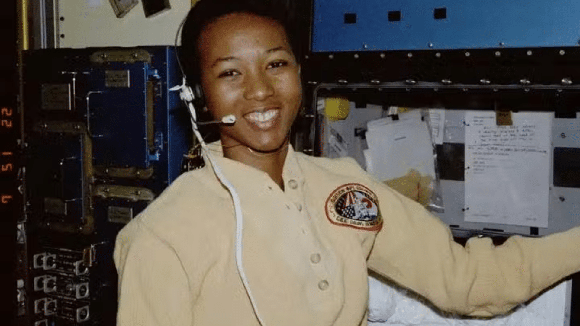 Astronaut Mae Jemison wearing a headset inside a spacecraft cabin with technical panels and notes visible