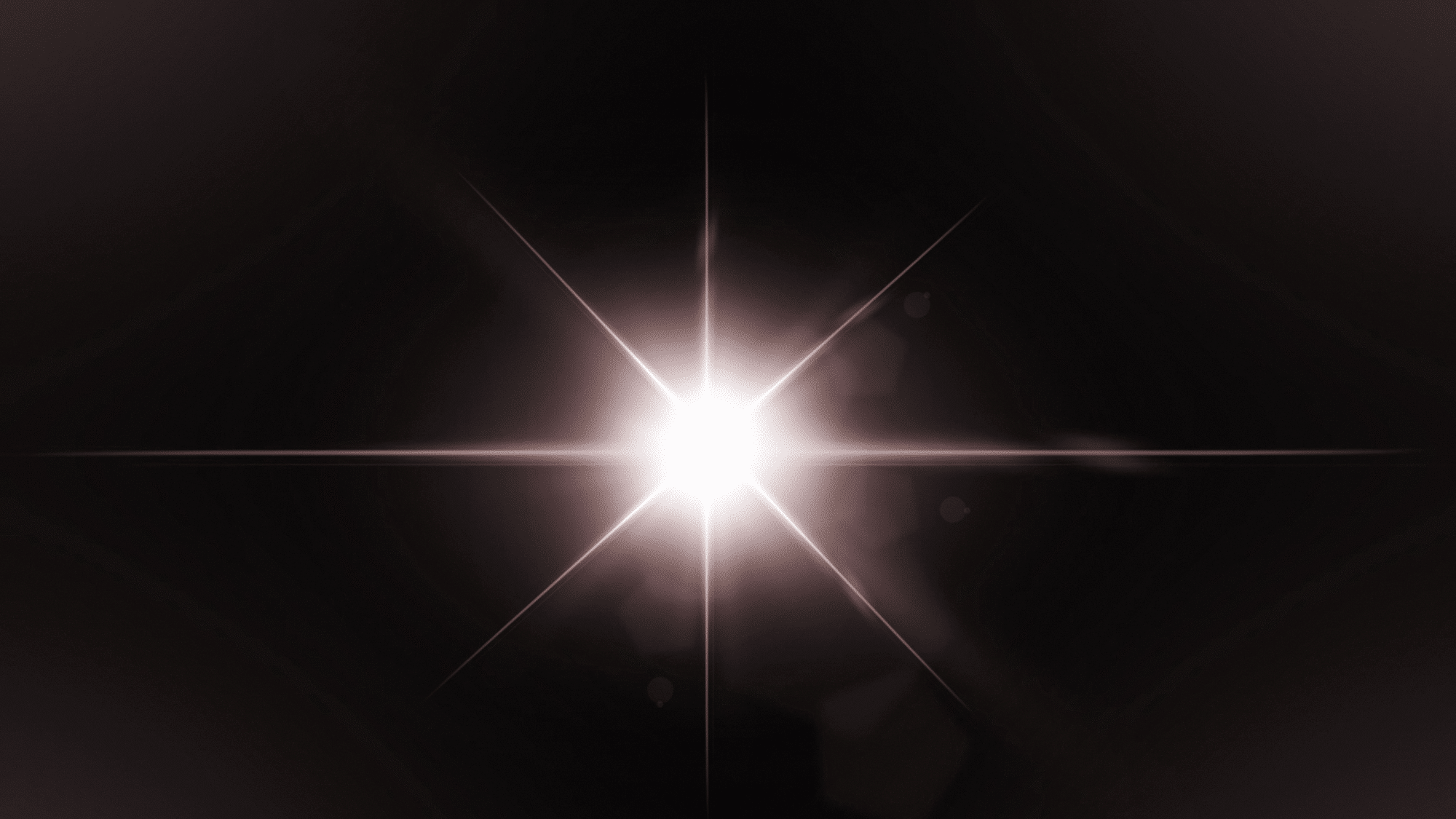 Bright white starburst lens flare centered against a dark background with radiating light streaks.
