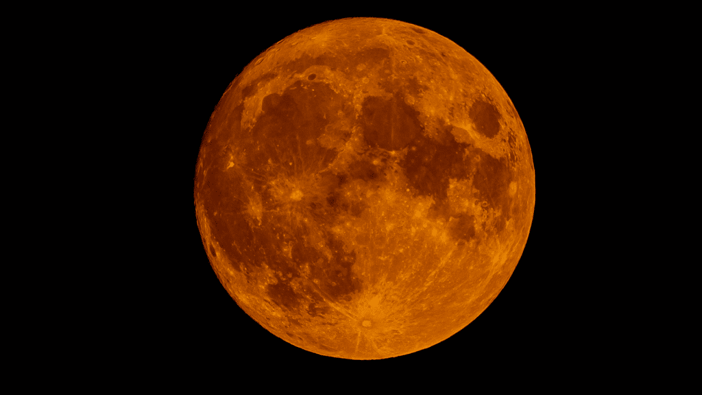 Close-up image of a deeply orange and red Moon against a black night sky, showing surface details and a few distant stars