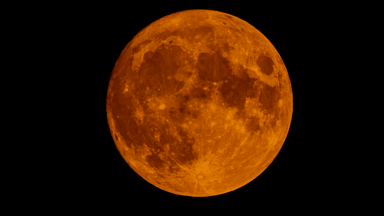 Close-up image of a deeply orange and red Moon against a black night sky, showing surface details and a few distant stars