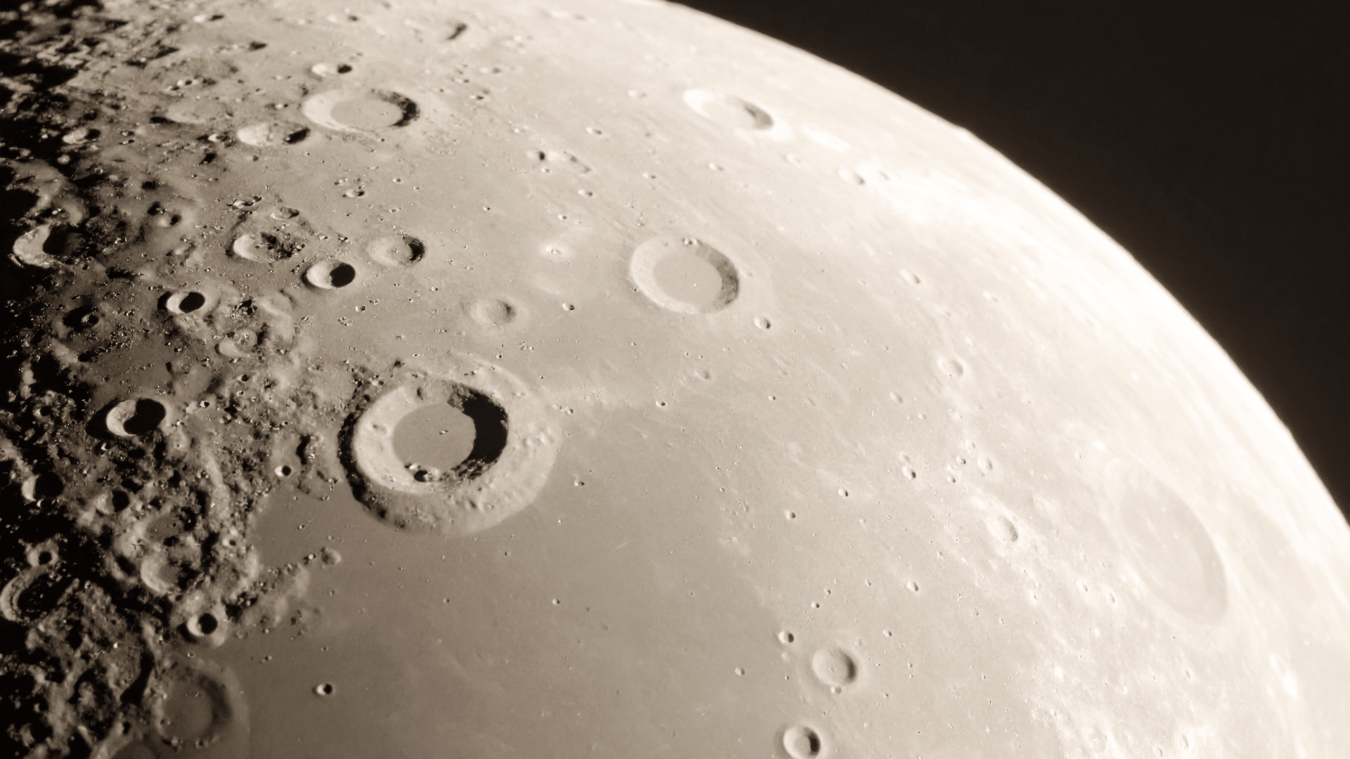 Close-up telescopic view of the heavily cratered, curved surface of the Moon transitioning into the blackness of space
