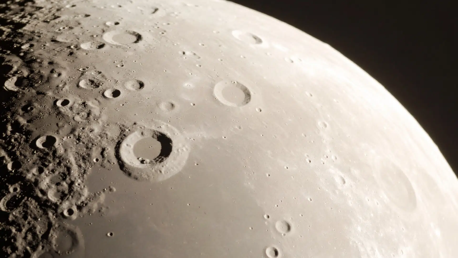 Close-up telescopic view of the heavily cratered, curved surface of the Moon transitioning into the blackness of space