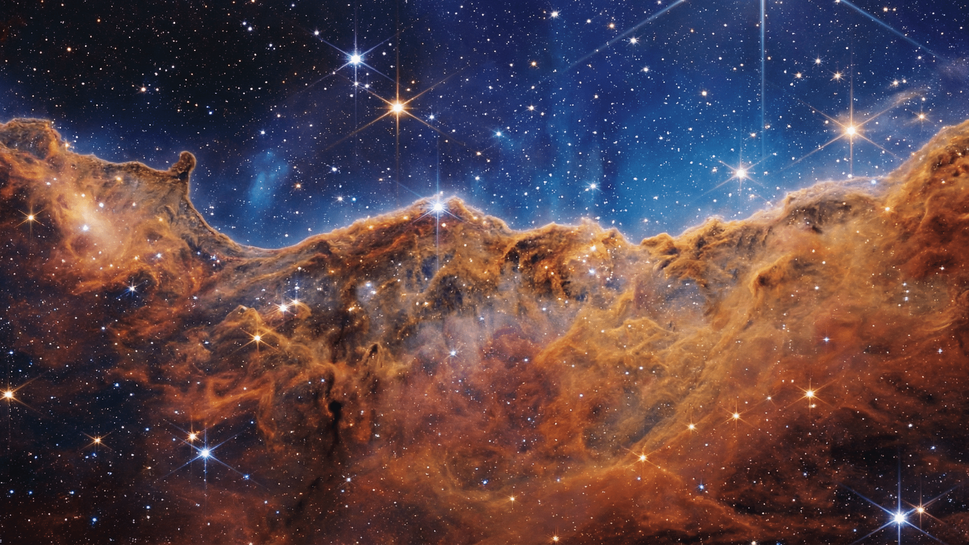 James Webb Telescope infrared view of the Carina Nebula’s cosmic cliffs with bright stars against a dark blue space background