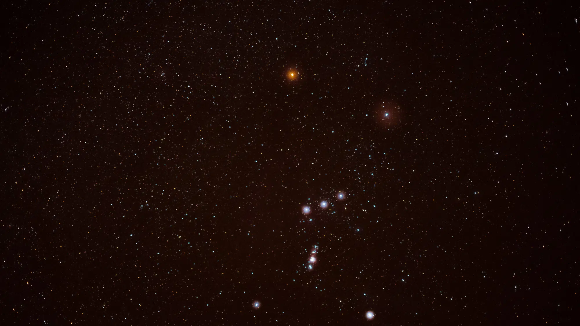 Long exposure photograph of the constellation Orion featuring Betelgeuse and the three stars of Orion's Belt against a dark, star-filled night sky.