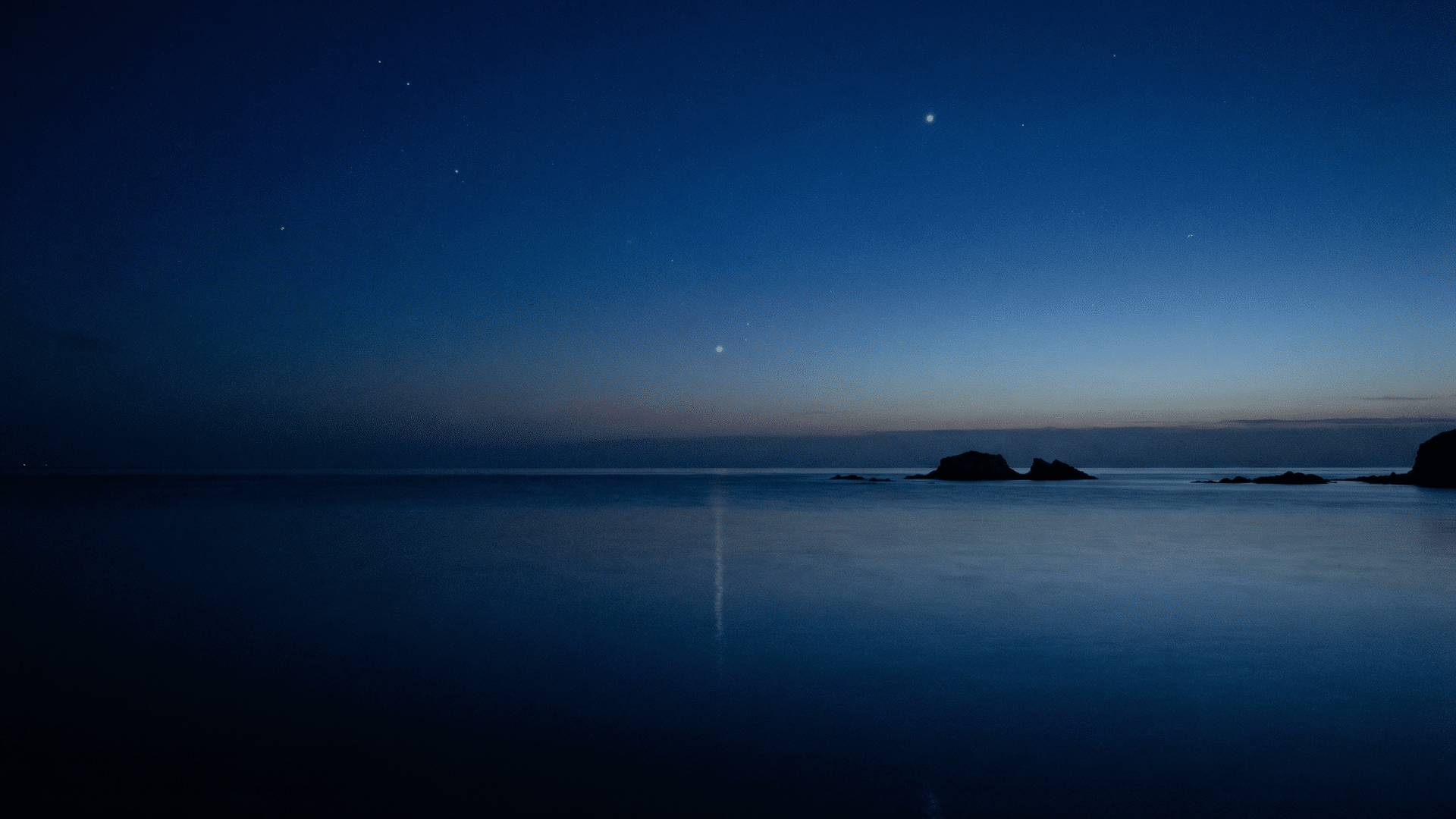 Ocean scene during nautical twilight, deep blue sky, faint horizon line visible, first bright stars appearing, subtle reflection on water