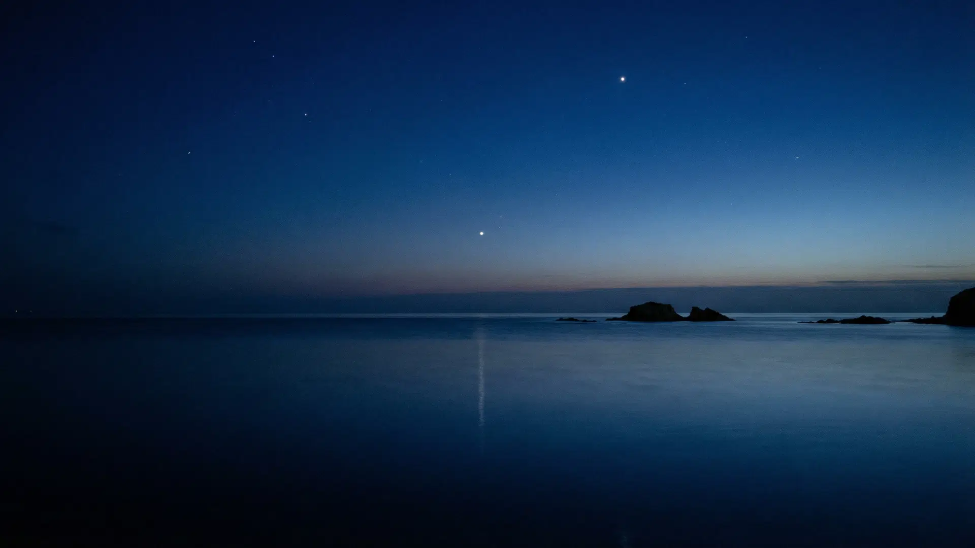 Ocean scene during nautical twilight, deep blue sky, faint horizon line visible, first bright stars appearing, subtle reflection on water