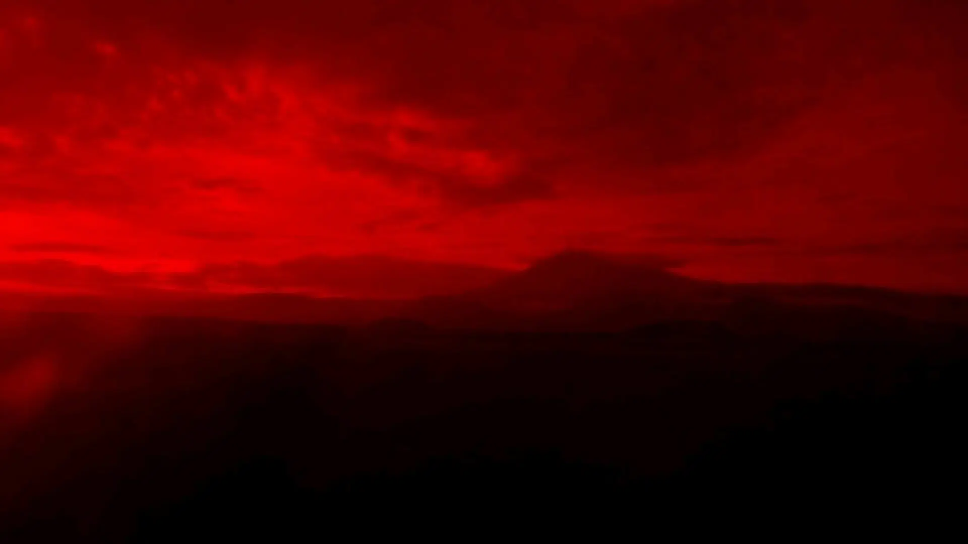 Silhouetted mountain range under an intensely vibrant red, cloudy night sky