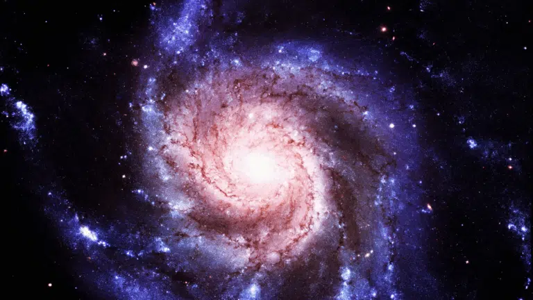 Vibrant spiral galaxy showcasing a bright white-pink core with blue star-forming regions against the black expanse of space.