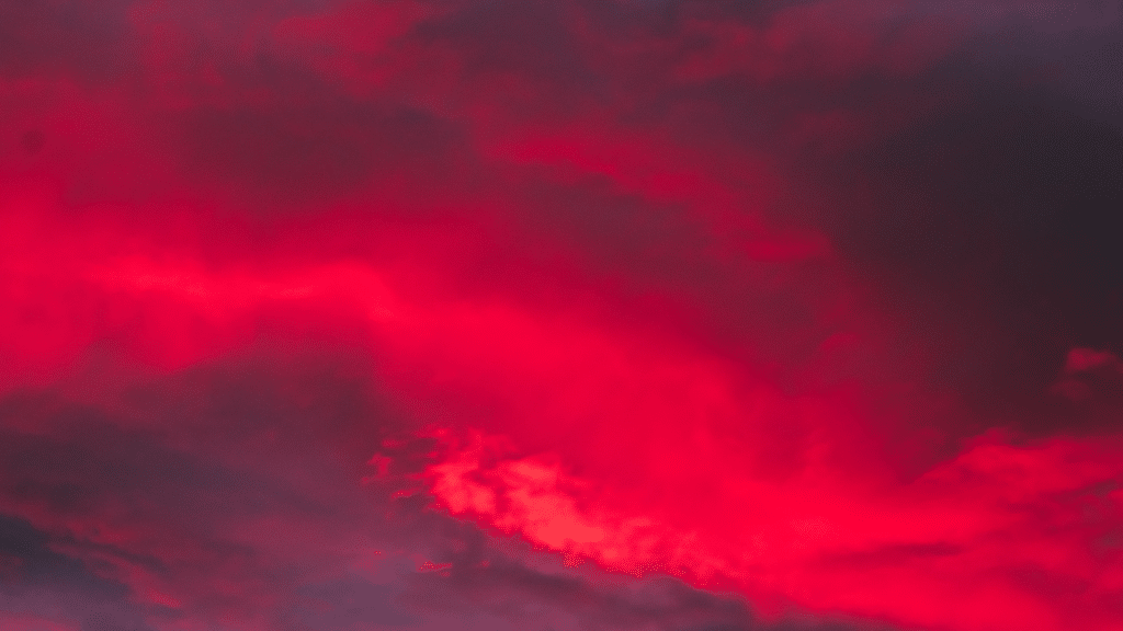 Vivid, saturated red clouds dominate a dark, dramatic sunset or twilight sky