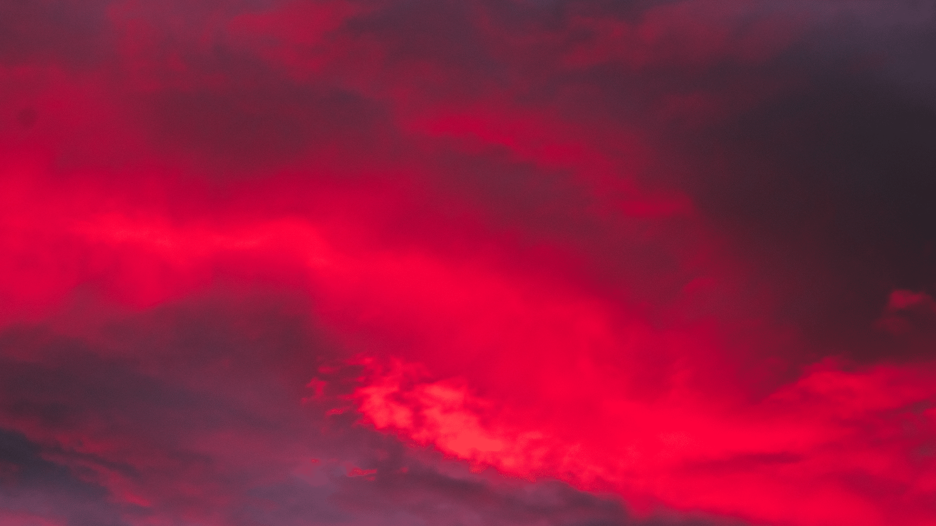 Vivid, saturated red clouds dominate a dark, dramatic sunset or twilight sky