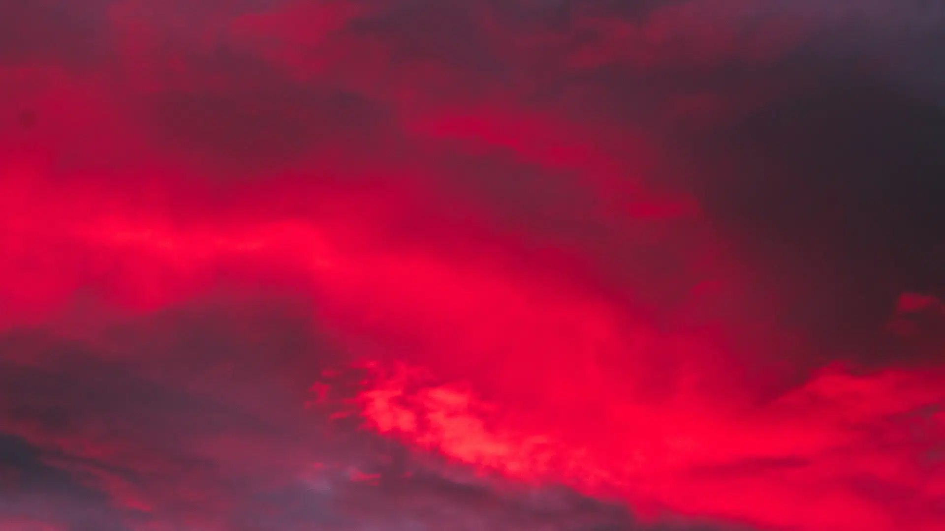 Vivid, saturated red clouds dominate a dark, dramatic sunset or twilight sky