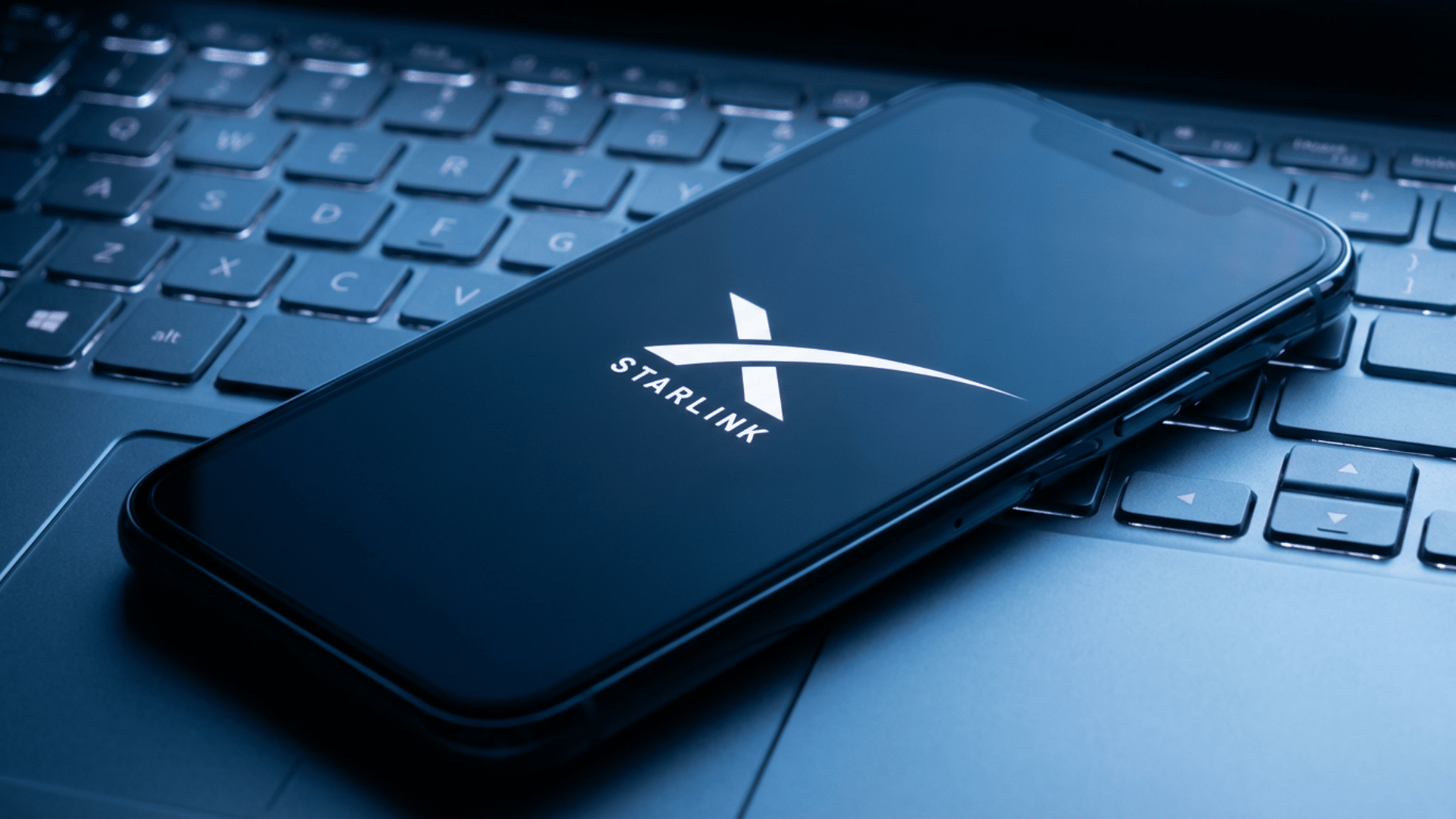 A smartphone displaying the Starlink logo is placed on a laptop keyboard.