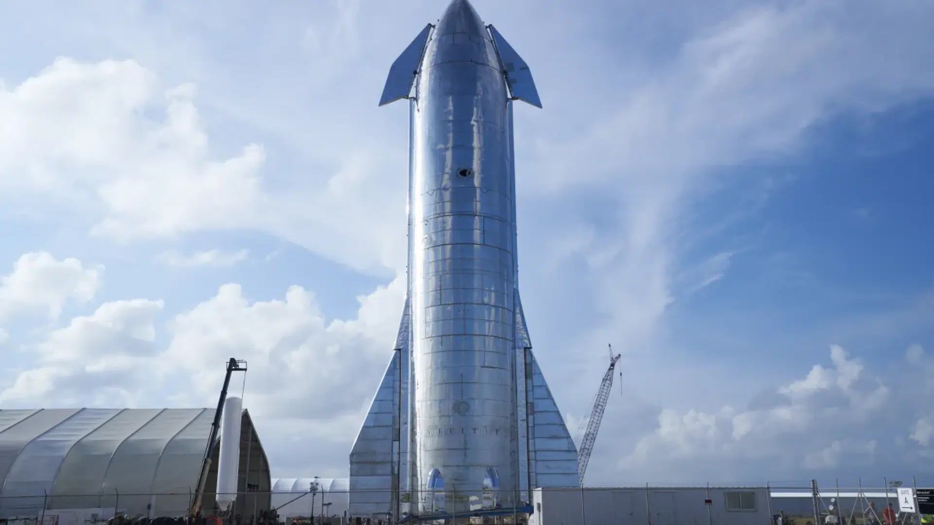 A tall, polished stainless steel SpaceX Starship stands vertically outdoors