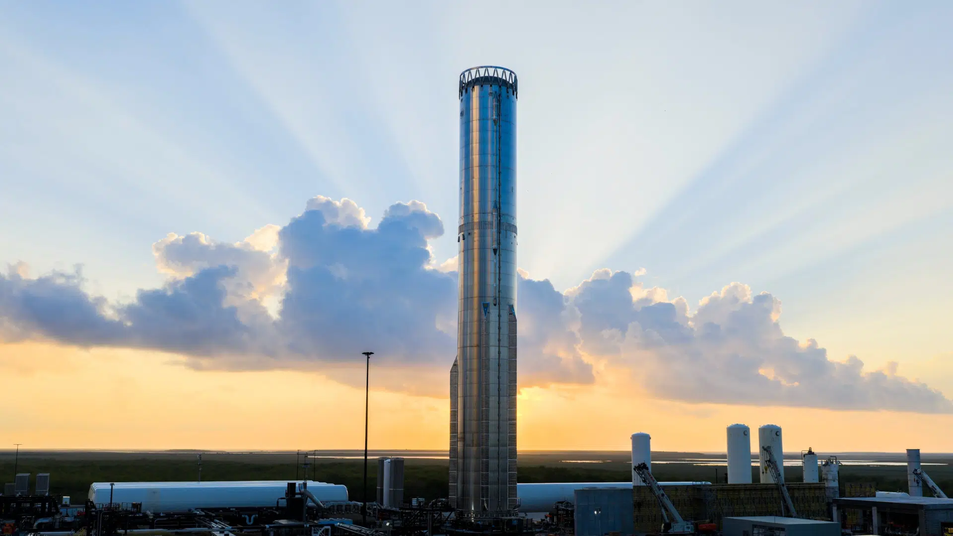 A tall, stainless steel SpaceX Starship prototype stands vertically against a dramatic sunset sky