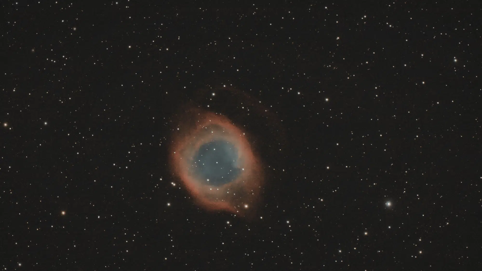 The Ring Nebula (M57) appears as a pale blue and reddish-orange celestial ring set against a dark, star-filled black space background.