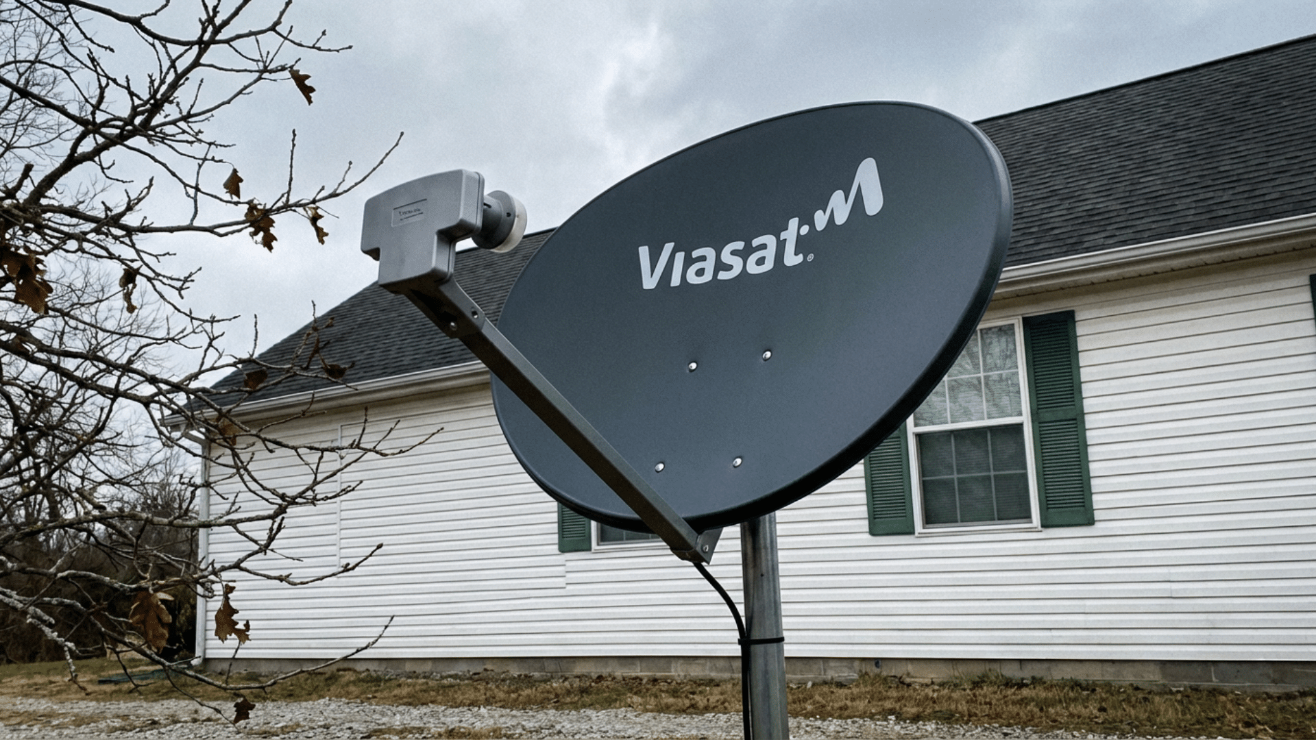 Viasat satellite dish mounted on a pole in front of a light-colored, vinyl-sided house