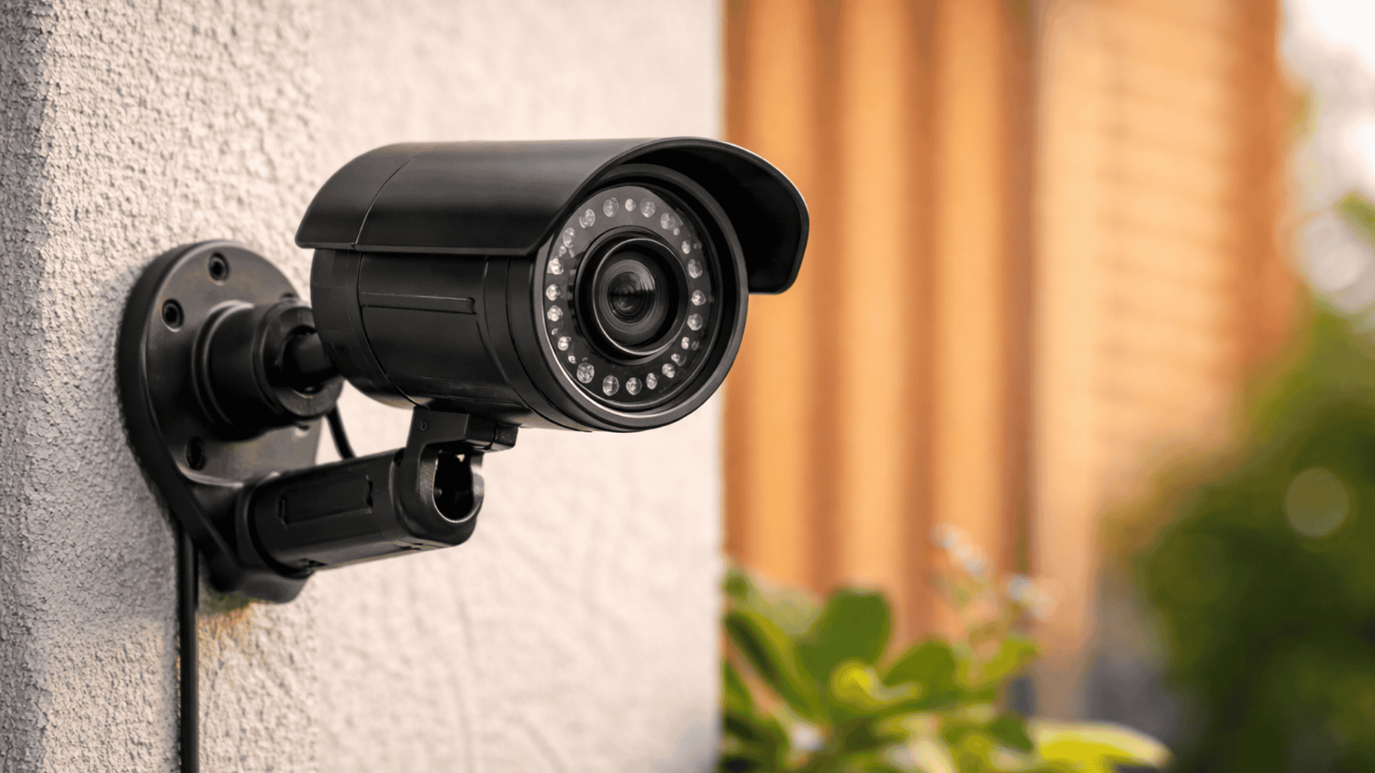 Close-up of a black security camera mounted on a wall with blurred background