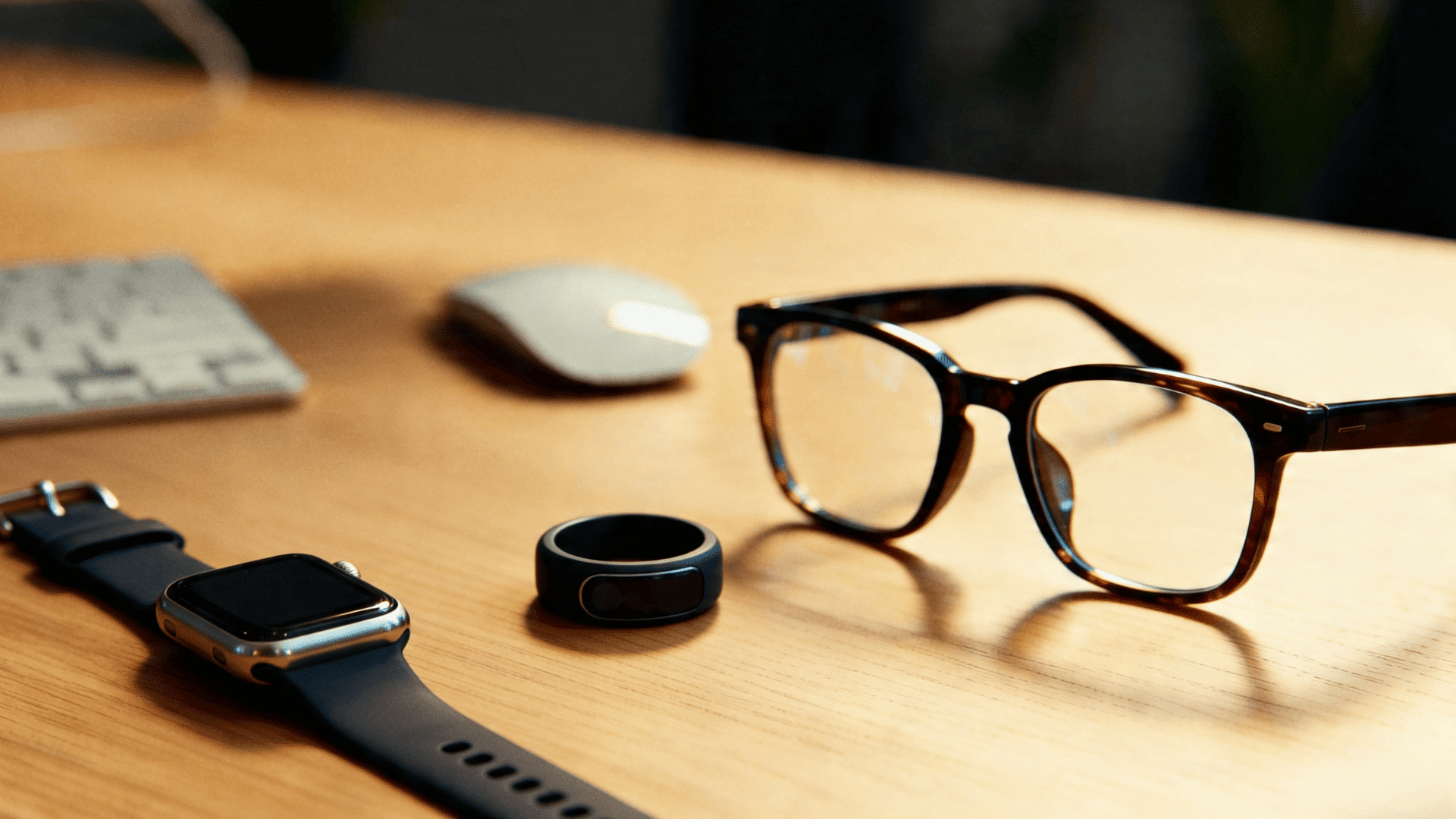 Close-up of smartwatch, smart ring, and eyeglasses on desk, representing wearable tech devices in a clean workspace setting.