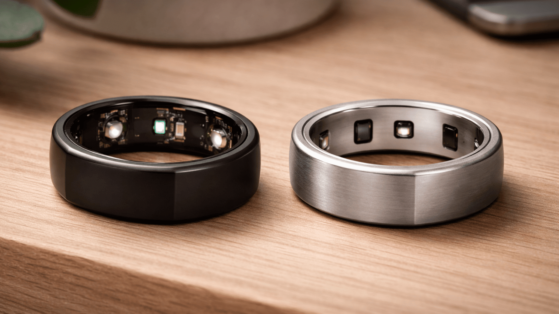_ Oura rings in black and silver finishes displayed side by side, showing sleek design and inner sensors on a wooden surface