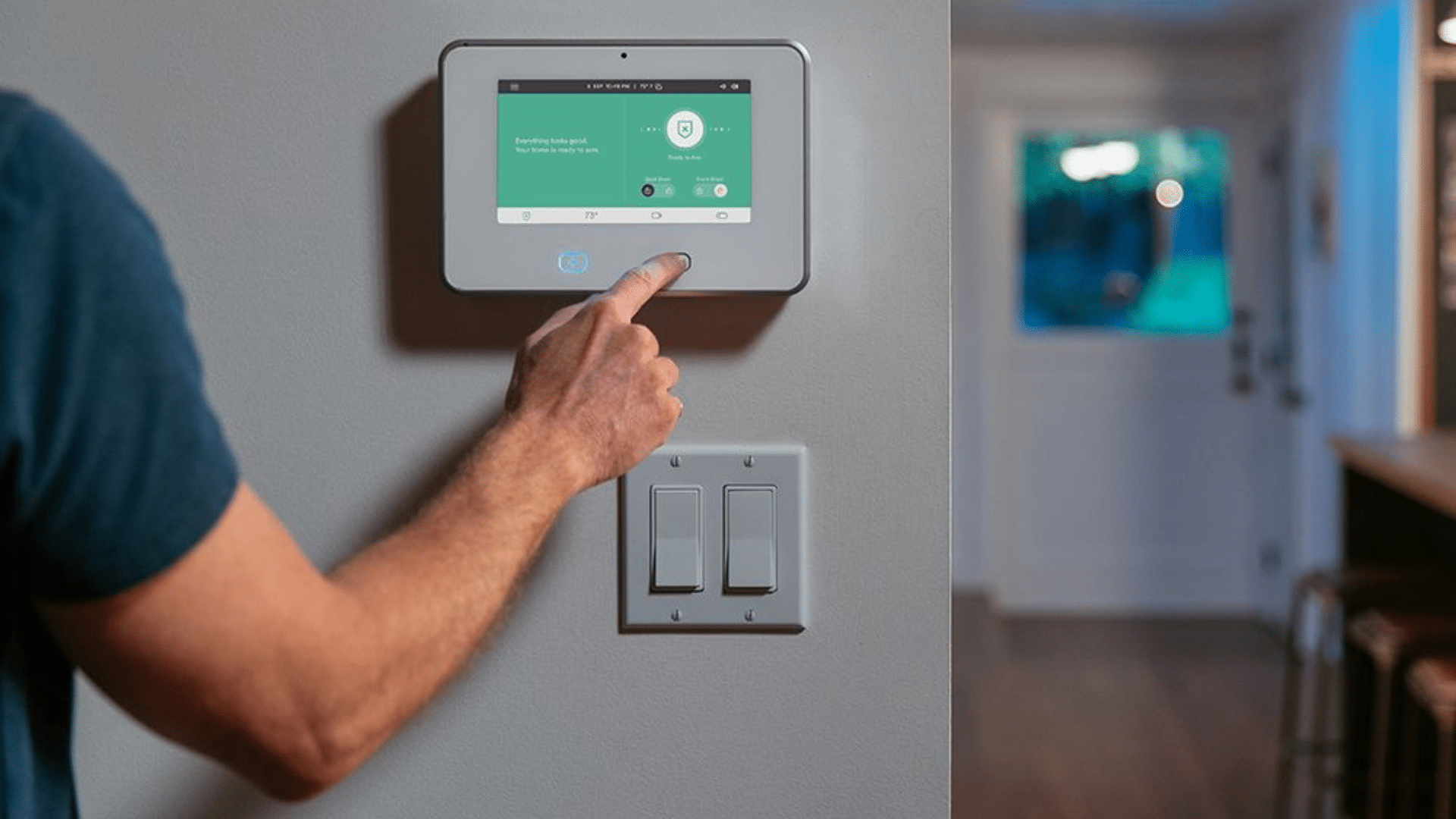 Person using Vivint smart home control panel mounted on wall with green interface next to light switches