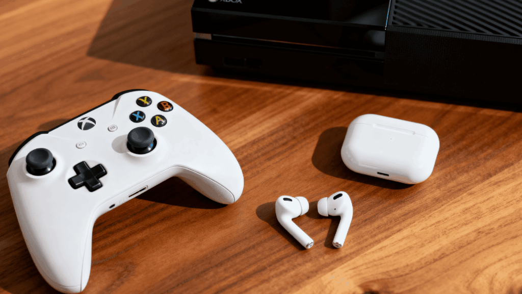 Xbox console with controller and wireless earbuds on a wooden table