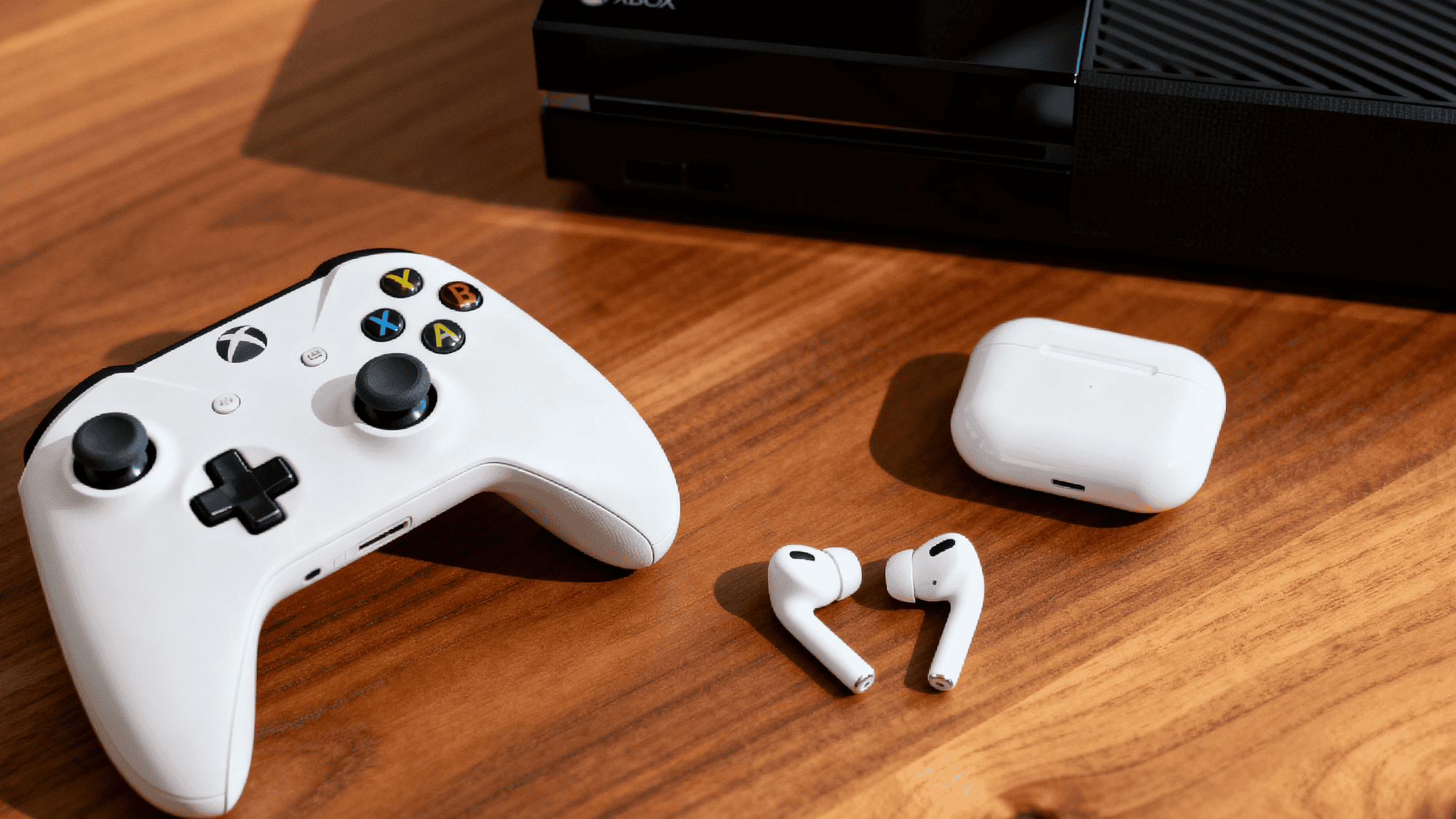 Xbox console with controller and wireless earbuds on a wooden table