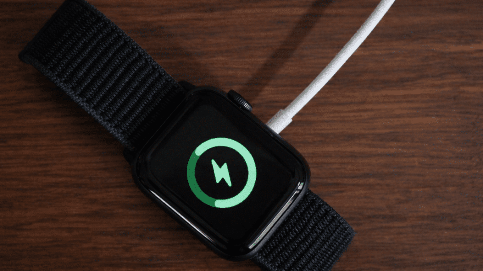 apple watch dying very quickly so put on charging shown with low battery icon on screen resting on dark wood surface with black band