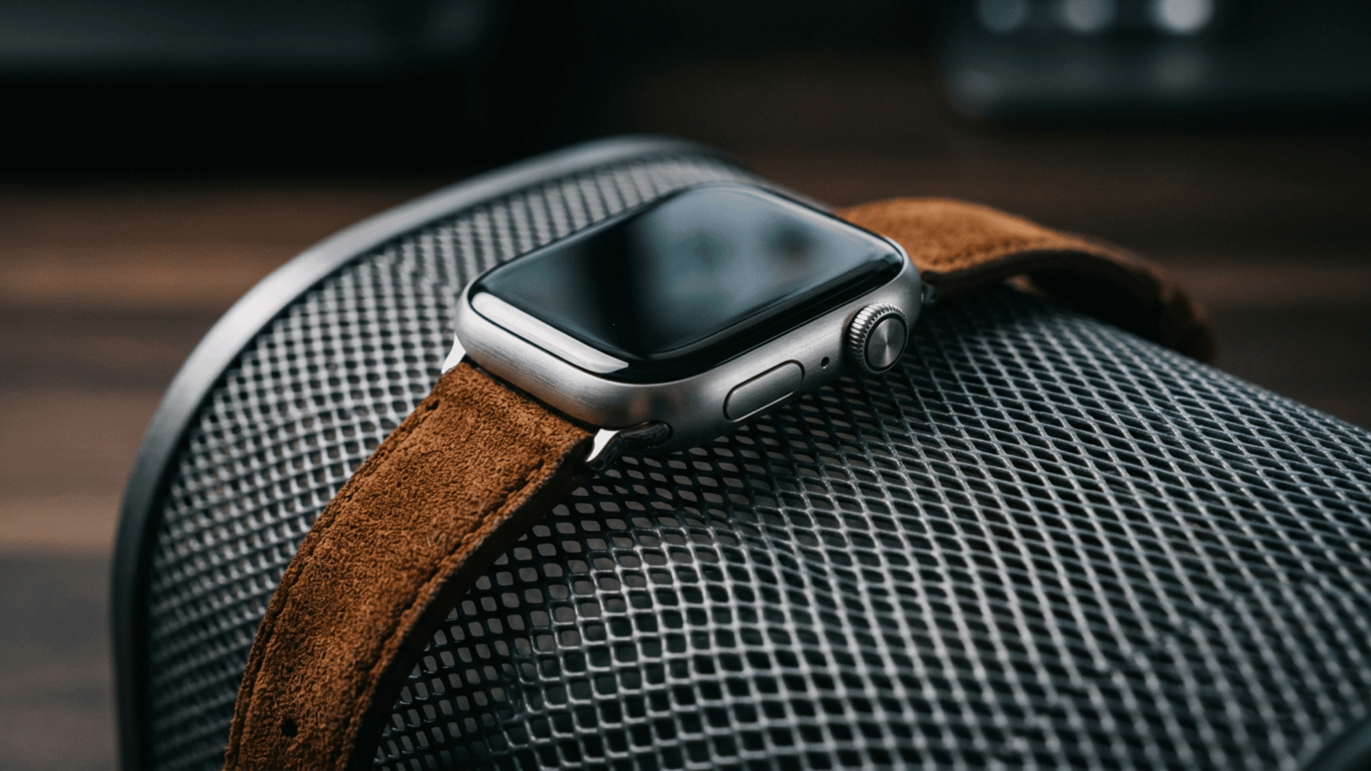 Apple Watch with brown suede leather band resting on chair arm close-up view