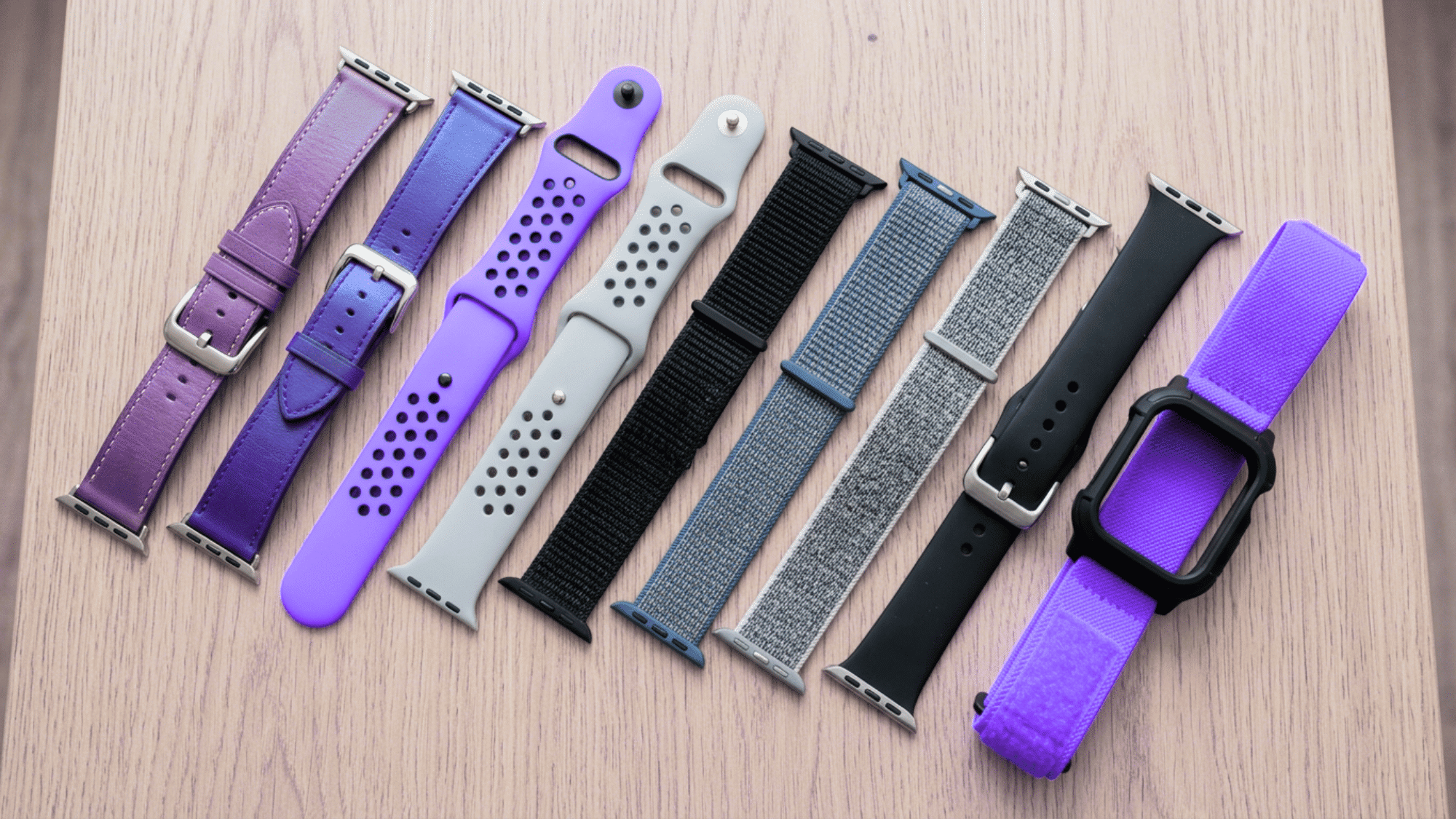 Collection of Apple Watch bands in leather, silicone, nylon and fabric on wood surface