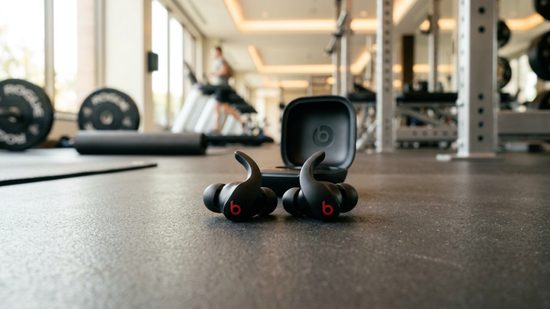 Powerbeats Fit wireless earbuds displayed on a gym surface with a clean and modern fitness background