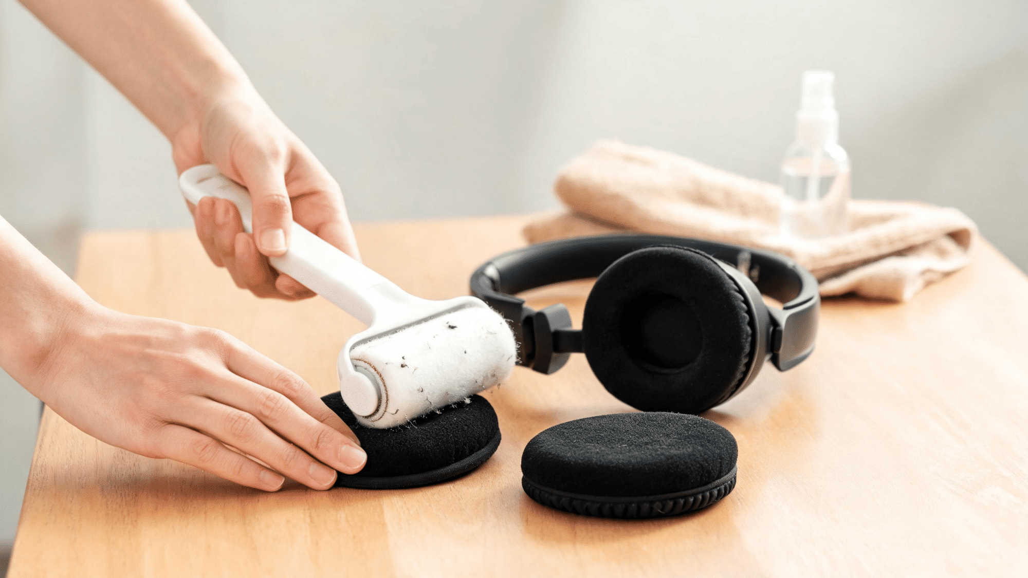 Lint roller removing debris from black velour headphone ear pads on table