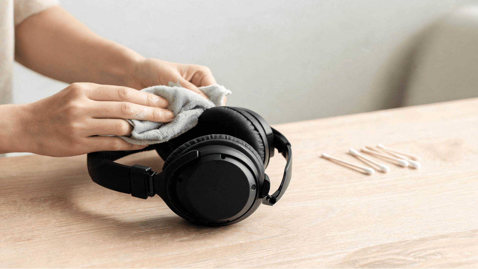 Cleaning detached leather ear pads with damp microfiber cloth on wood desk