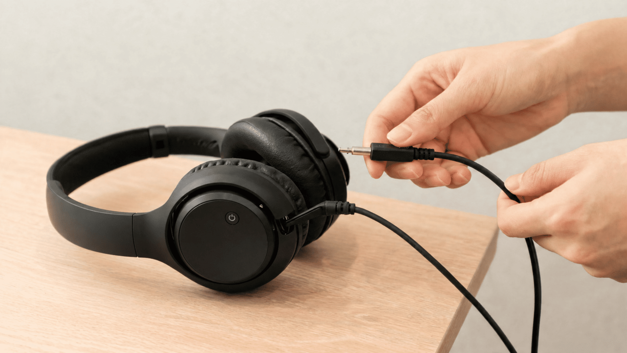 Unplugging 3.5mm audio cable from black over-ear headphones on wood table