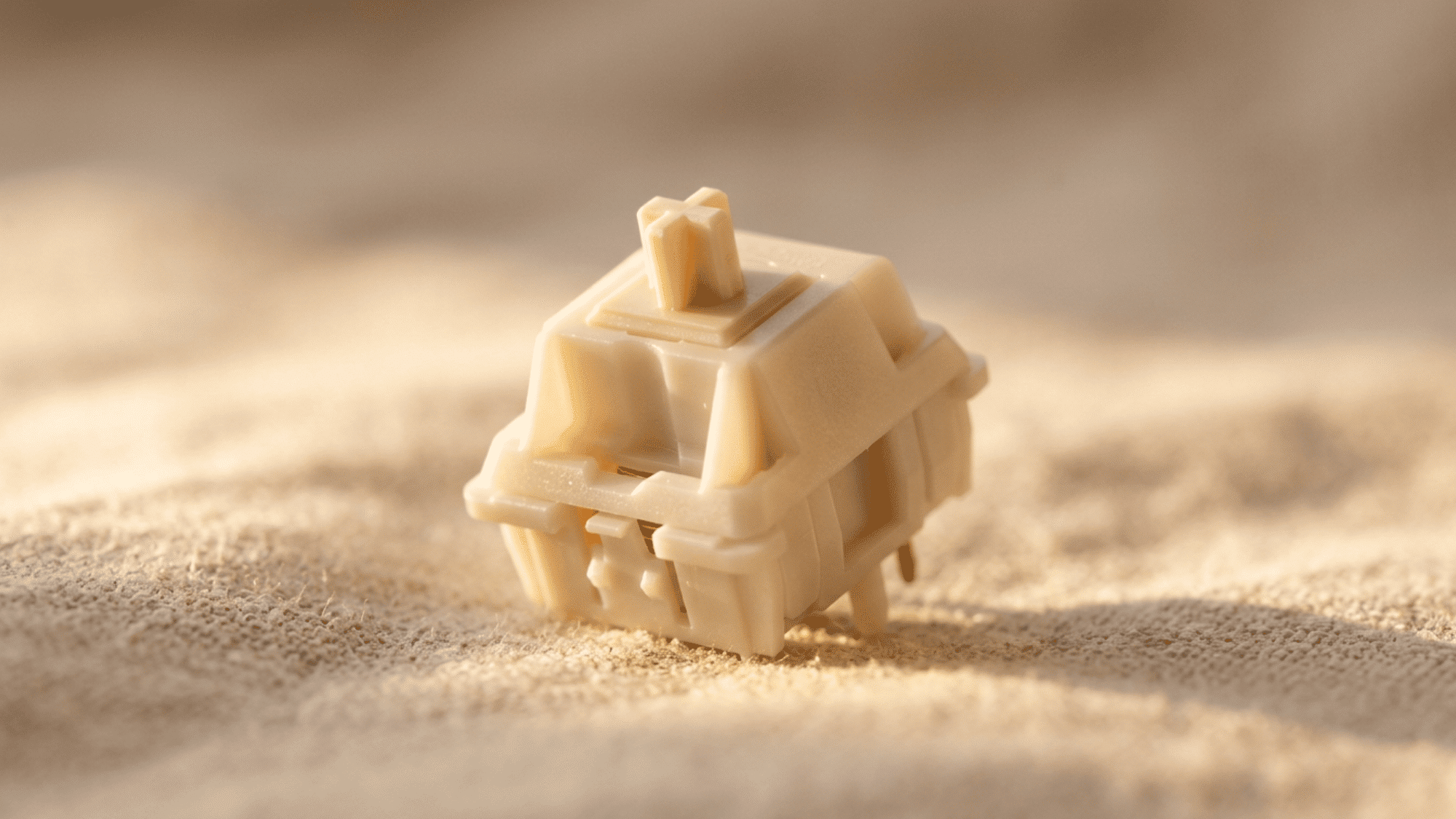 Cream-colored NovelKeys switch with translucent POM housing on a sandy fabric surface