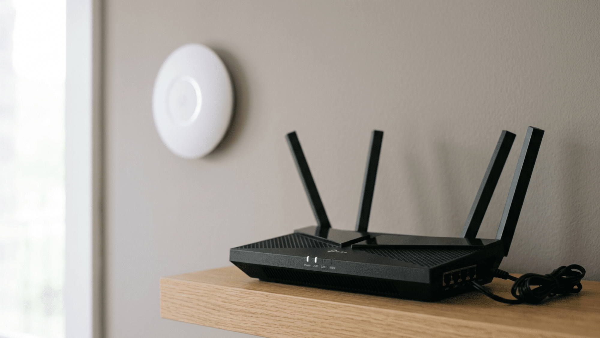Black Wi-Fi router on wooden shelf with white access point mounted on wall nearby