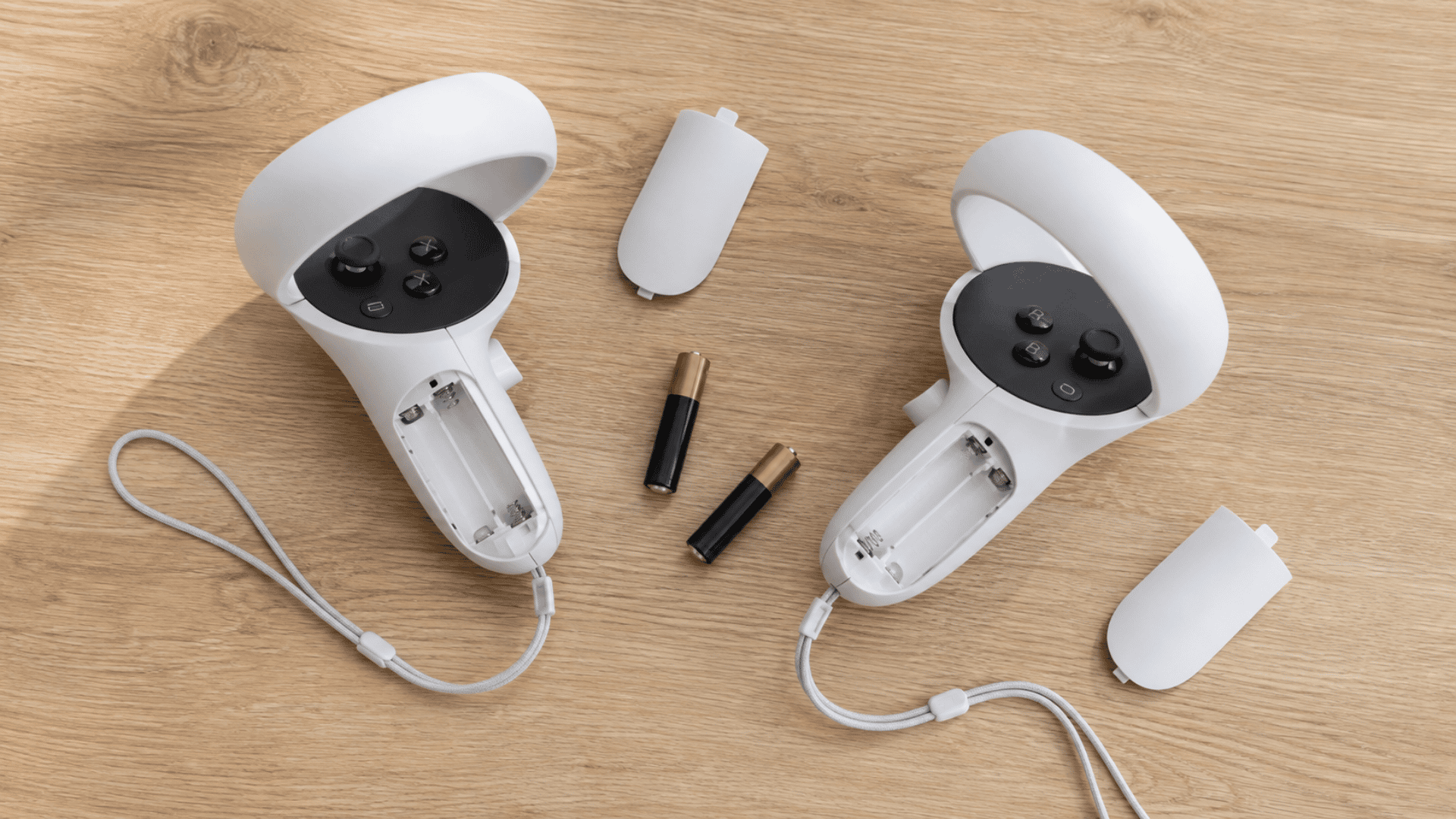 Meta Quest 3 controllers with open battery compartments and AA batteries on a table