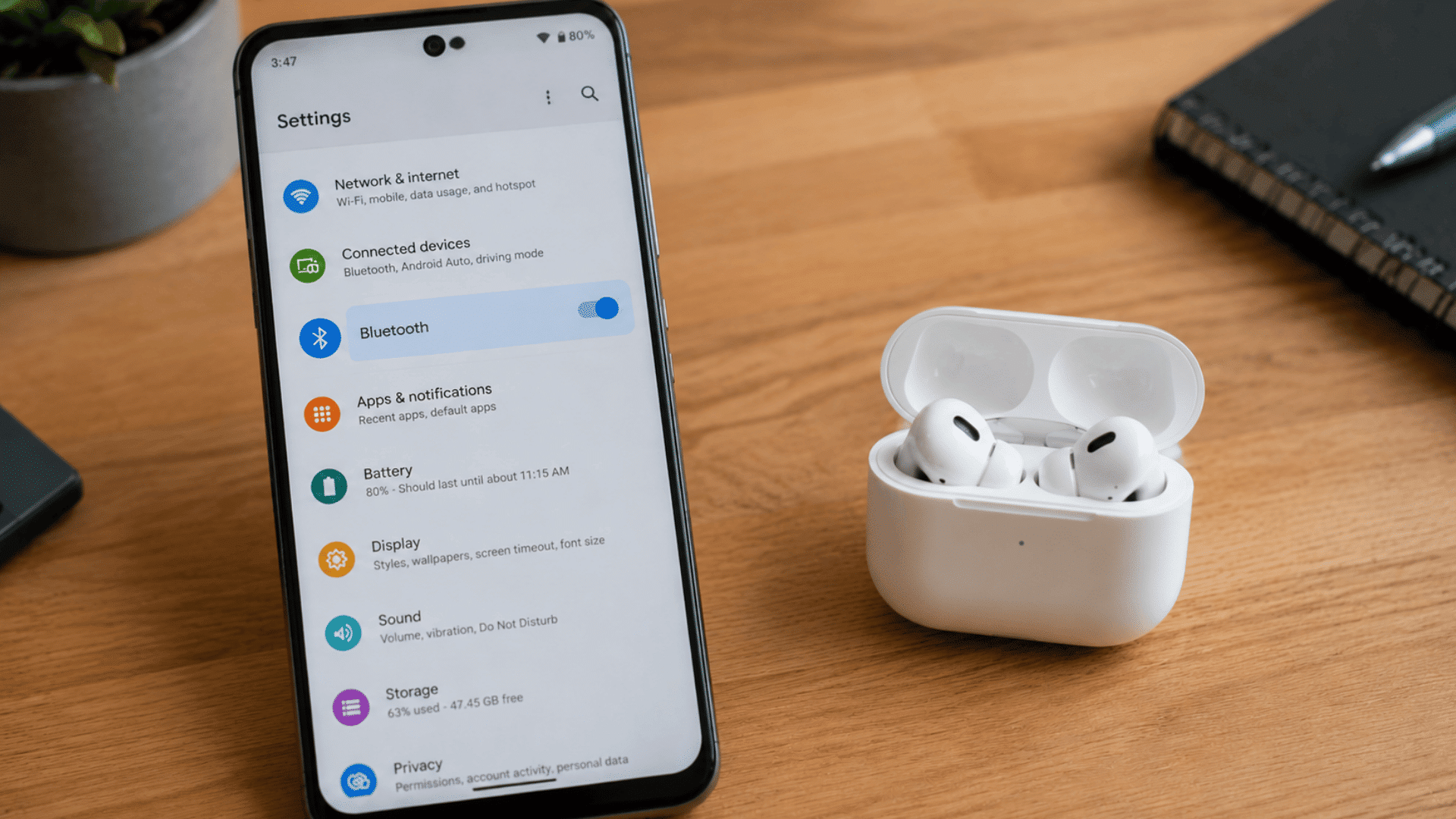 open AirPods case with earbuds inside next to an Android phone Bluetooth menu